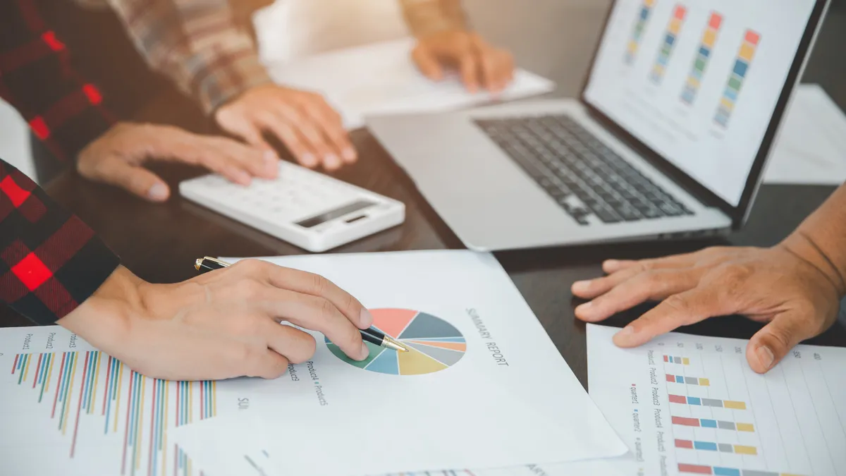 Business people leaning over a table together analyzing charts and graphs.